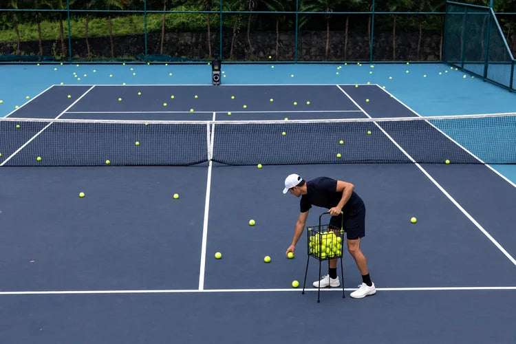 Tennis player collecting scattered balls with a hopper while TERO Pro stands across the court