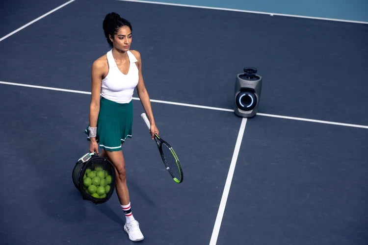 Tennis player carrying a ball bag beside a Lumistar TERO Pro tennis robot.